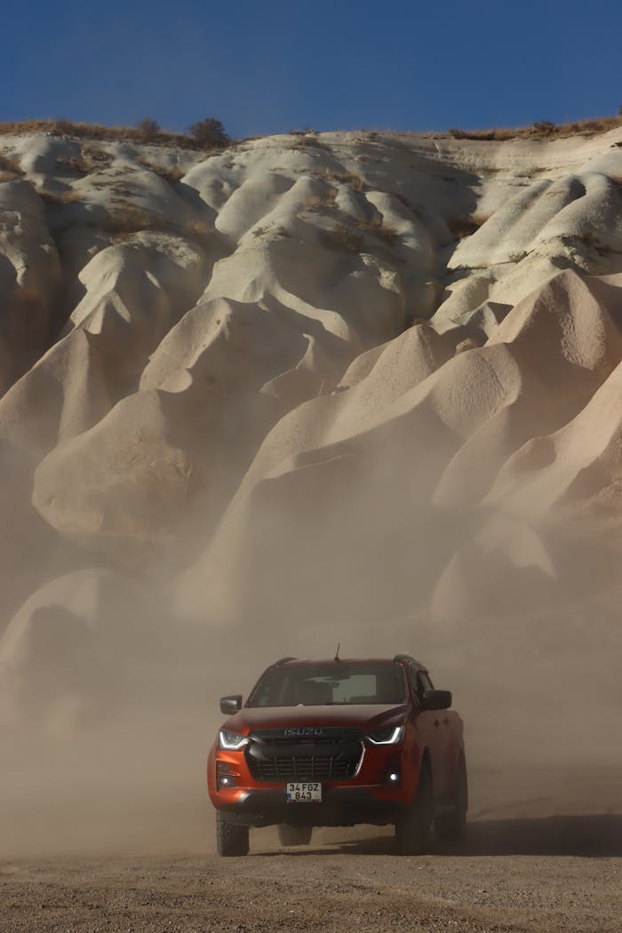 An Isuzu pickup truck navigating the sandy dunes against dramatic rock formations, stirring dust.