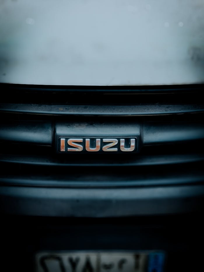 Detailed close-up of Isuzu logo on a vehicle grill during daytime.